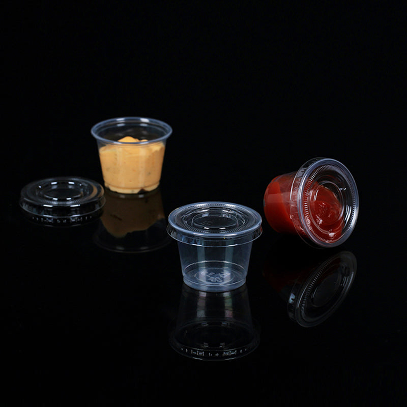 1 oz disposable plastic portion cups on black background, two filled with ketchup and mustard sauces