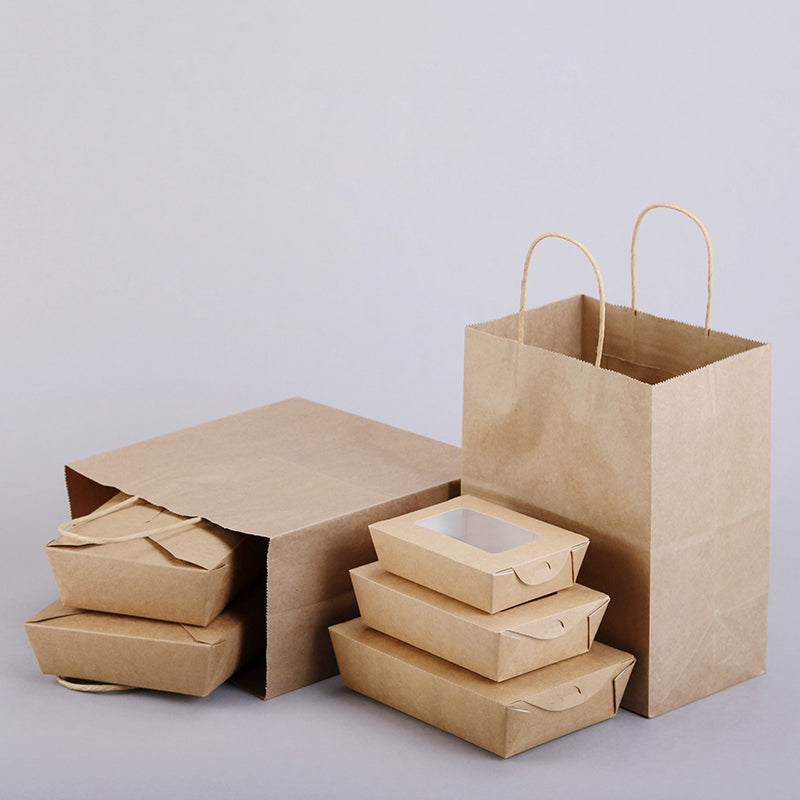 PHB12710 medium kraft brown paper bags with handles placed on a table beside paper boxes – perfect for cafes, bakeries, boutiques, and take out packaging