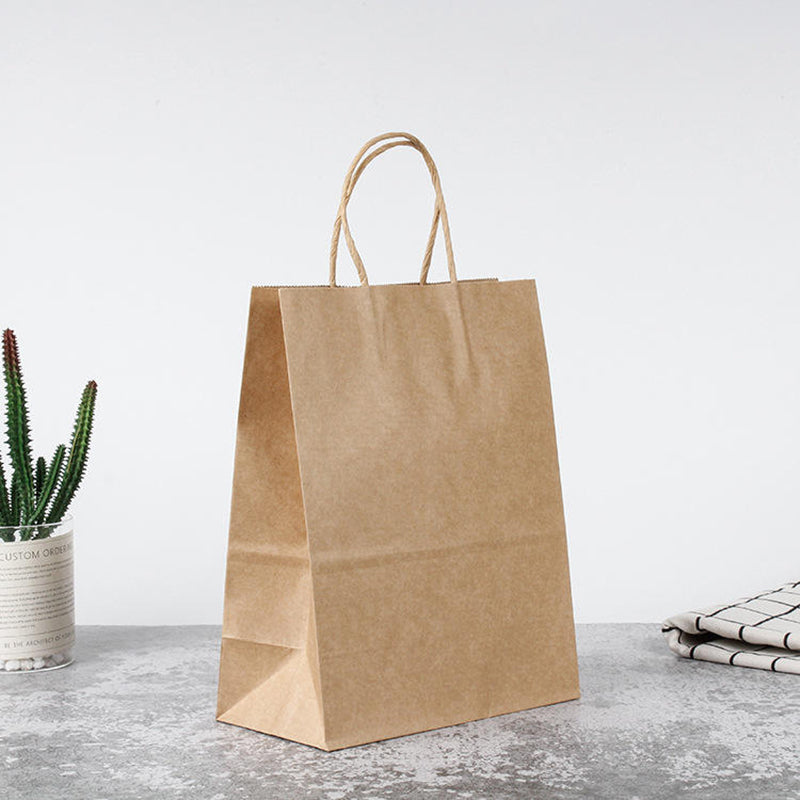PHB13510 kraft brown paper bags with handles displayed on a table – perfect for cafes, boutiques, groceries, and food delivery packaging